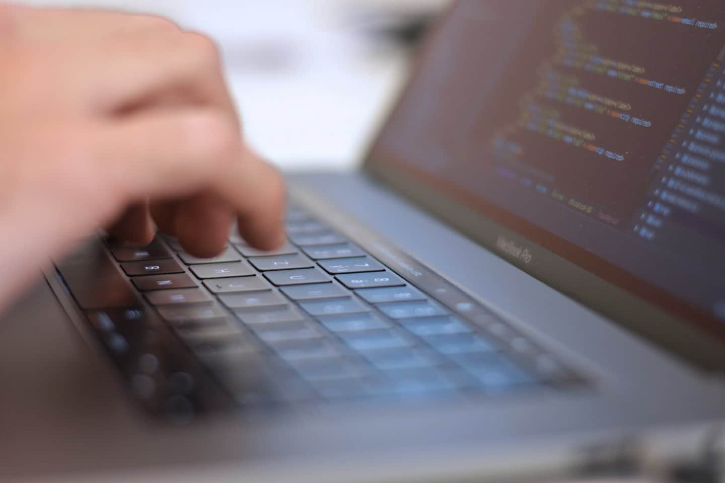 Mani che digitano righe di codice di programmazione su una tastiera di laptop.