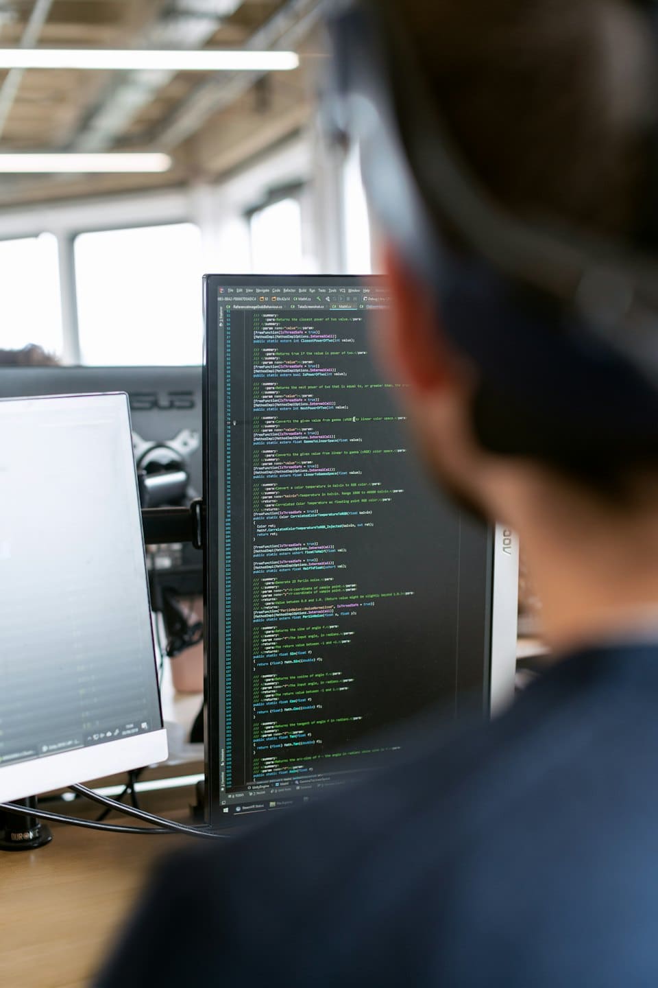 Programmatore concentrato sul codice su due monitor di computer.