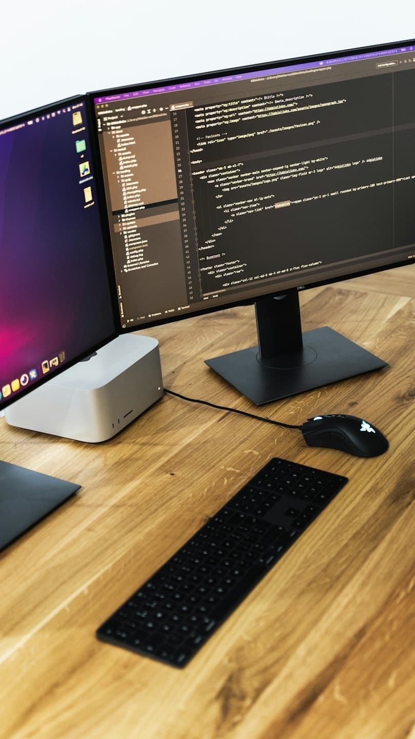 Due monitor di computer con codice su una scrivania di legno.